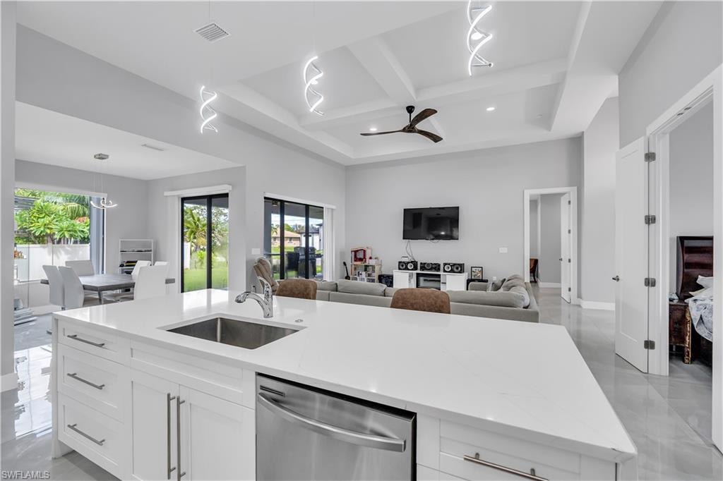 Kitchen with a kitchen island with sink, white cabinetry, hanging light fixtures, stainless steel dishwasher, and light stone countertops