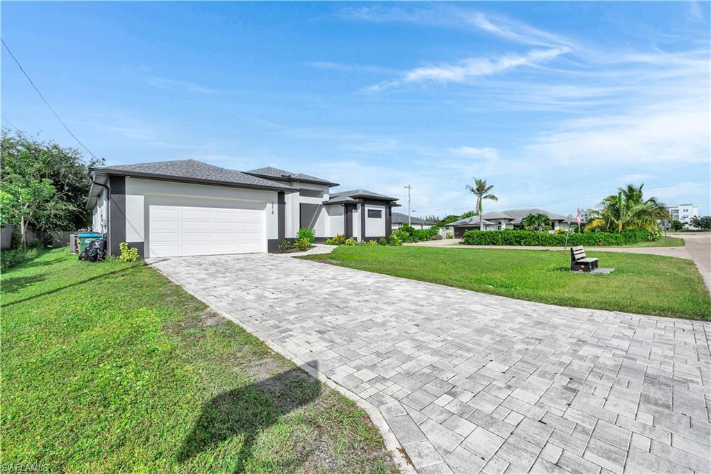 Prairie-style home with an attached garage, decorative driveway, a front yard, stucco siding, and roof with shingles