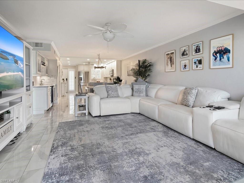 Living area featuring crown molding, light marble finish floors, a ceiling fan, and a chandelier
