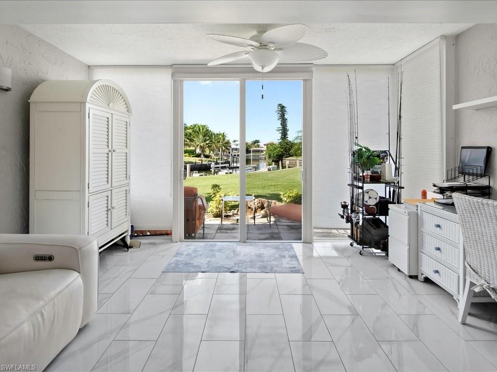 Entryway featuring a textured wall, ceiling fan, a water view, marble look tile flooring, and a wall of windows