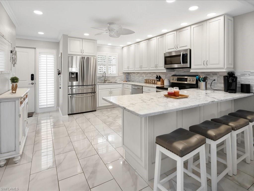 Kitchen with stainless steel appliances, white cabinetry, a peninsula, decorative backsplash, and ceiling fan