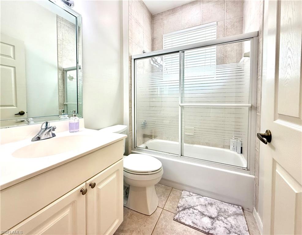 Full bath featuring shower / bath combination with glass door, vanity, and light tile patterned flooring
