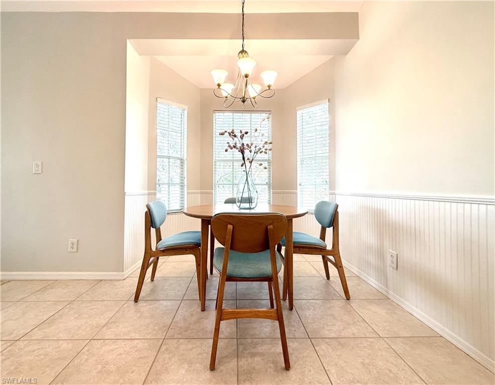 Dining area with light tile patterned floors, a wainscoted wall, and a chandelier