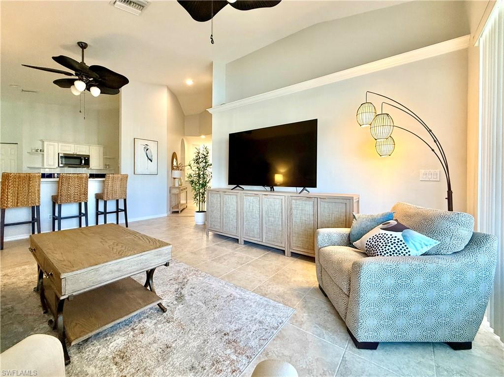 Living room featuring vaulted ceiling, a ceiling fan, and light tile patterned flooring