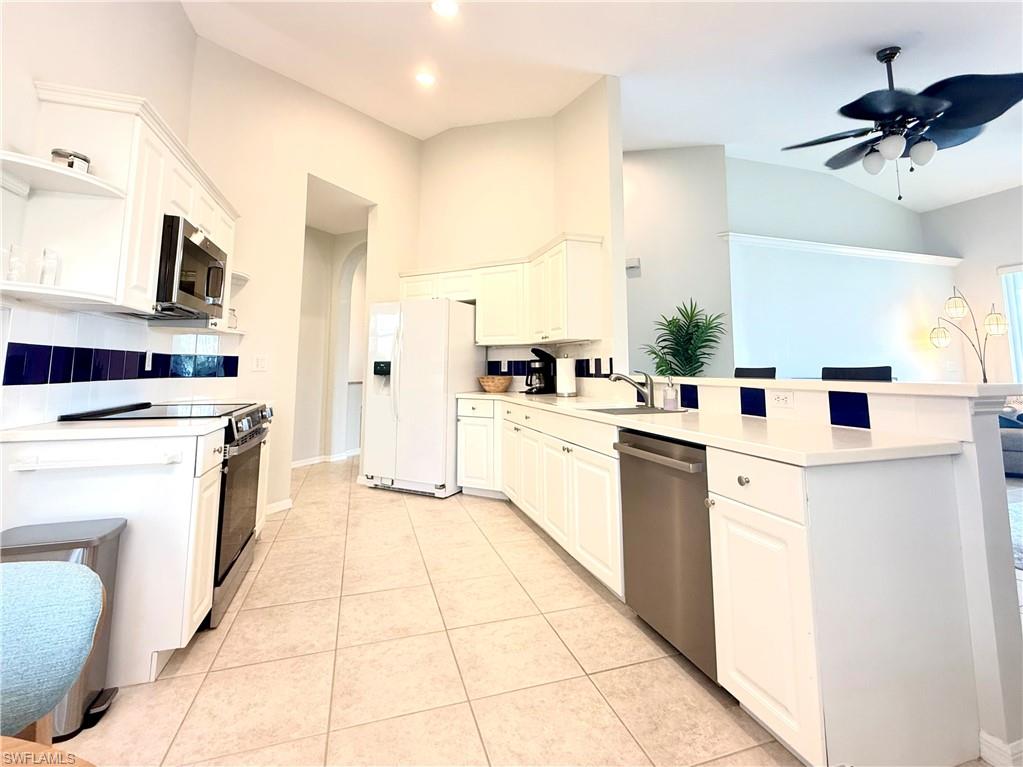 Kitchen with appliances with stainless steel finishes, white cabinetry, ceiling fan, recessed lighting, and vaulted ceiling