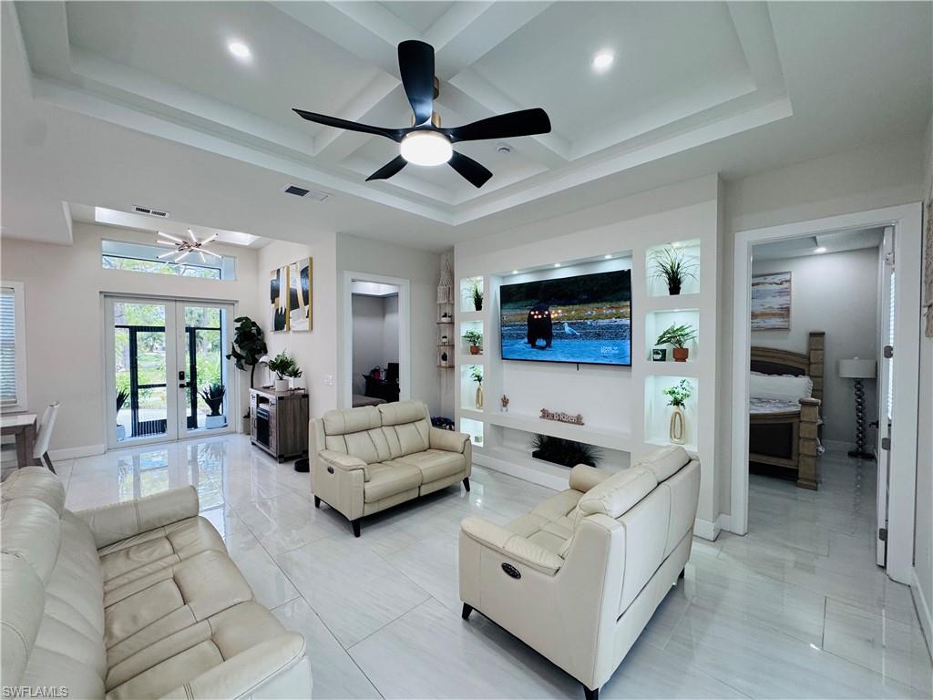 Living room featuring coffered ceiling, a ceiling fan, french doors, beamed ceiling, and light marble finish floors