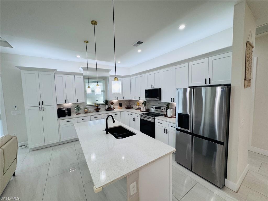 Kitchen featuring stainless steel appliances, white cabinets, light stone countertops, pendant lighting, and recessed lighting