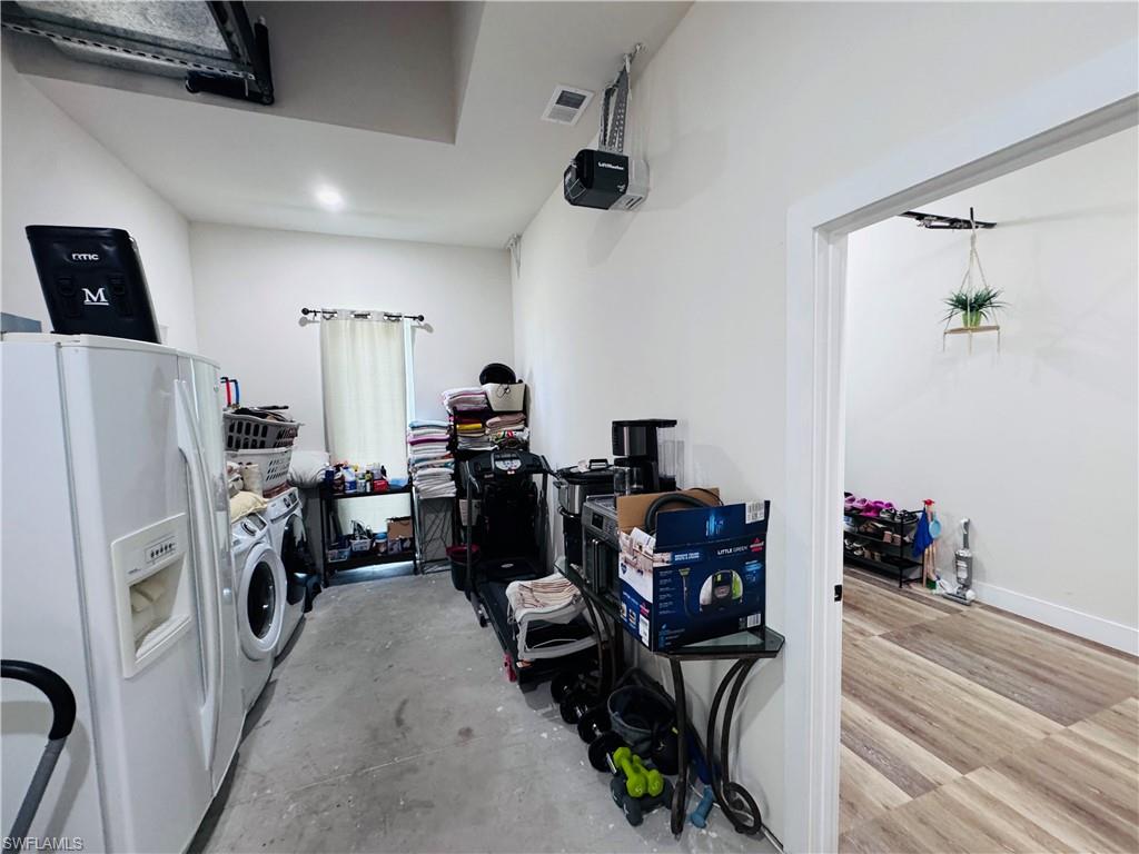 Garage featuring white fridge with ice dispenser, washing machine and clothes dryer, and a garage door opener
