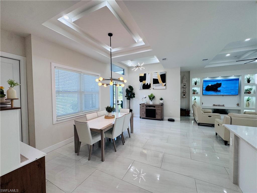 Dining room featuring a tray ceiling, a chandelier, and light marble finish flooring