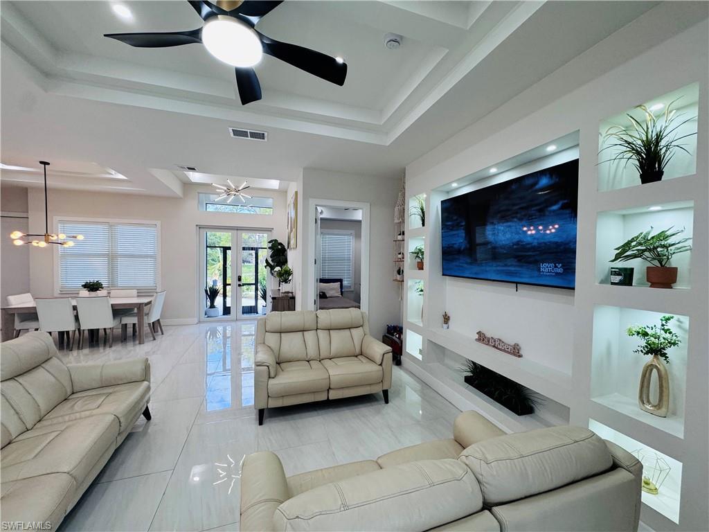 Living area with a raised ceiling, built in shelves, french doors, and a chandelier