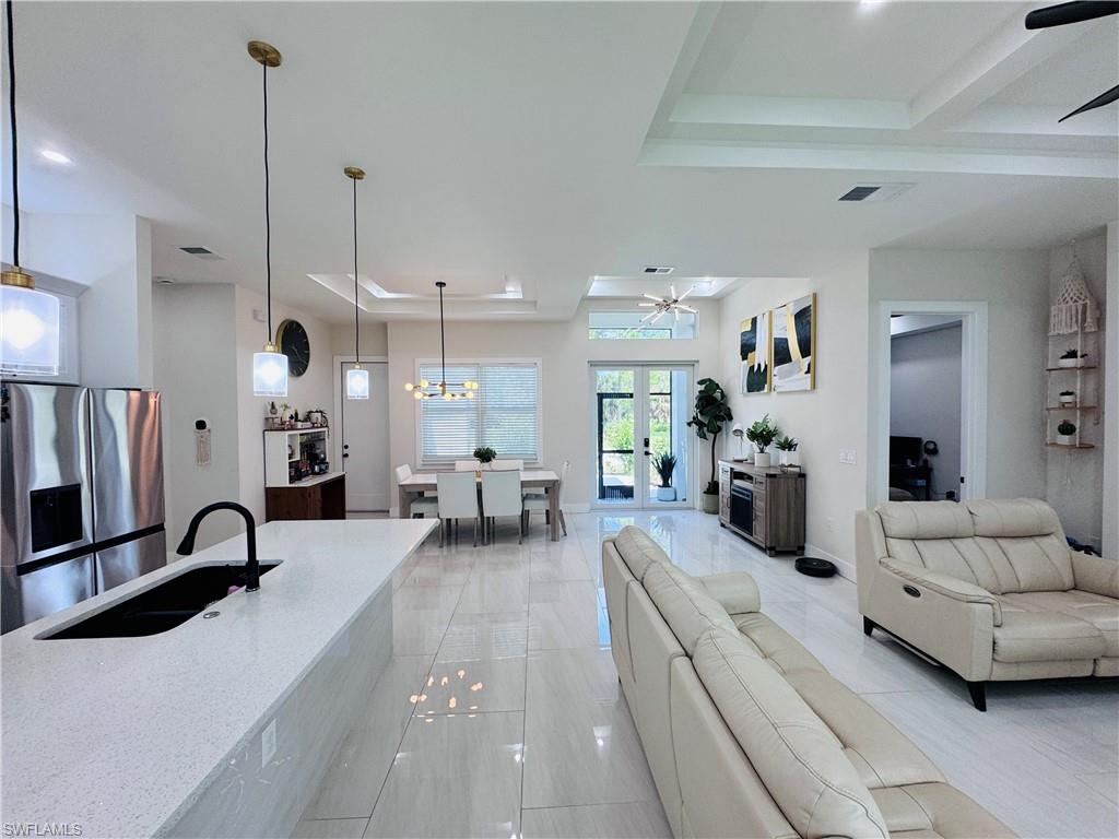 Living room featuring a raised ceiling, a ceiling fan, french doors, a chandelier, and beamed ceiling