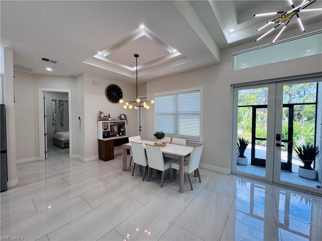 Dining area with a chandelier, a raised ceiling, and french doors
