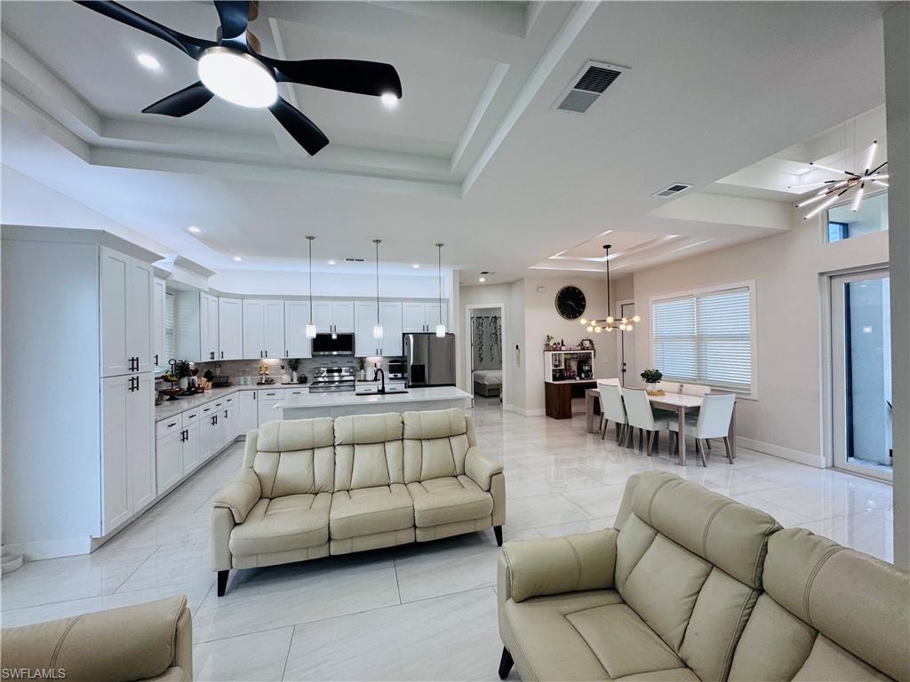 Living room featuring ceiling fan, a raised ceiling, a chandelier, and recessed lighting