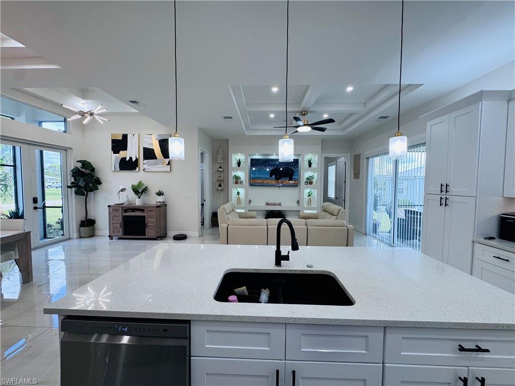 Kitchen featuring a ceiling fan, pendant lighting, open floor plan, light stone countertops, and beam ceiling