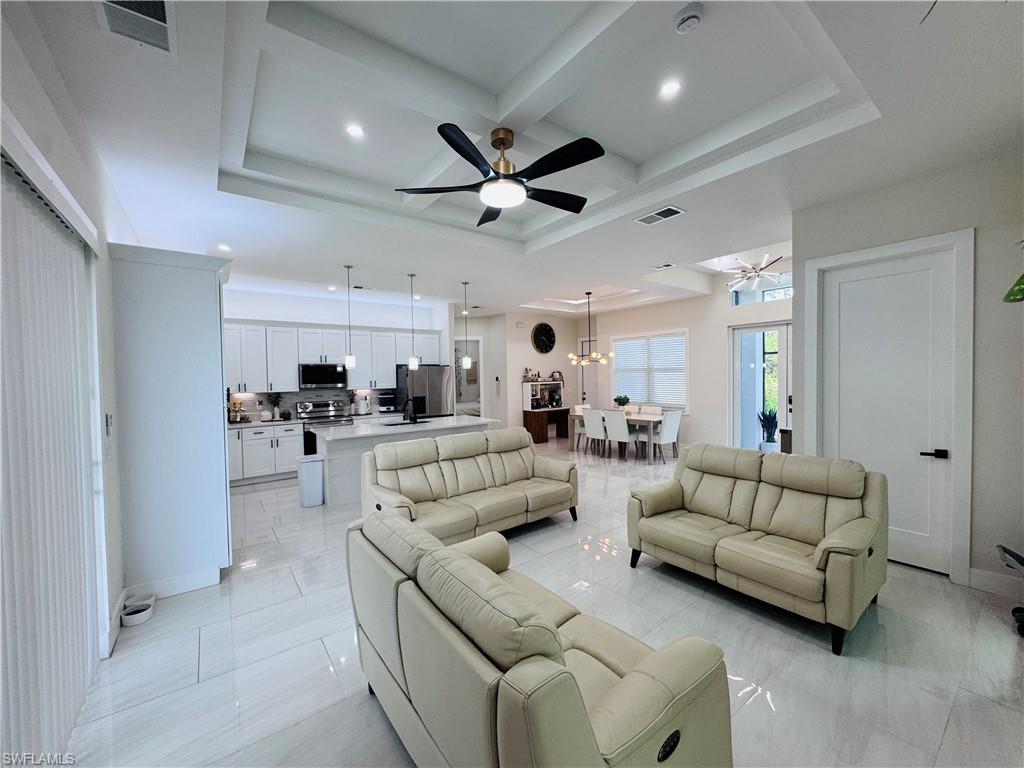 Living room with coffered ceiling, a ceiling fan, beam ceiling, a chandelier, and recessed lighting