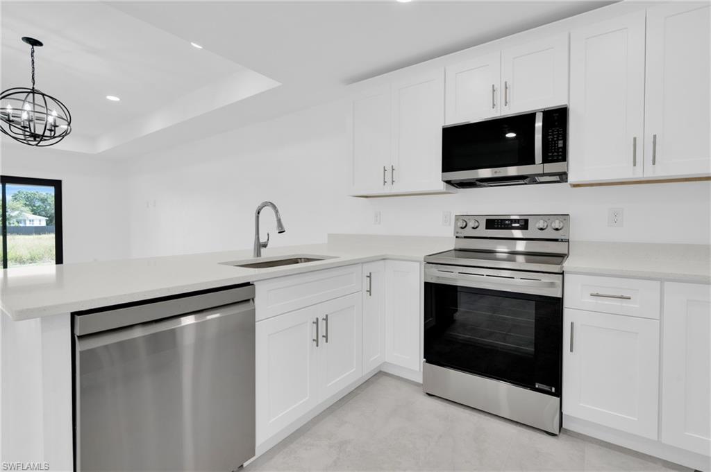 Kitchen with stainless steel appliances, white cabinets, a peninsula, light stone counters, and recessed lighting