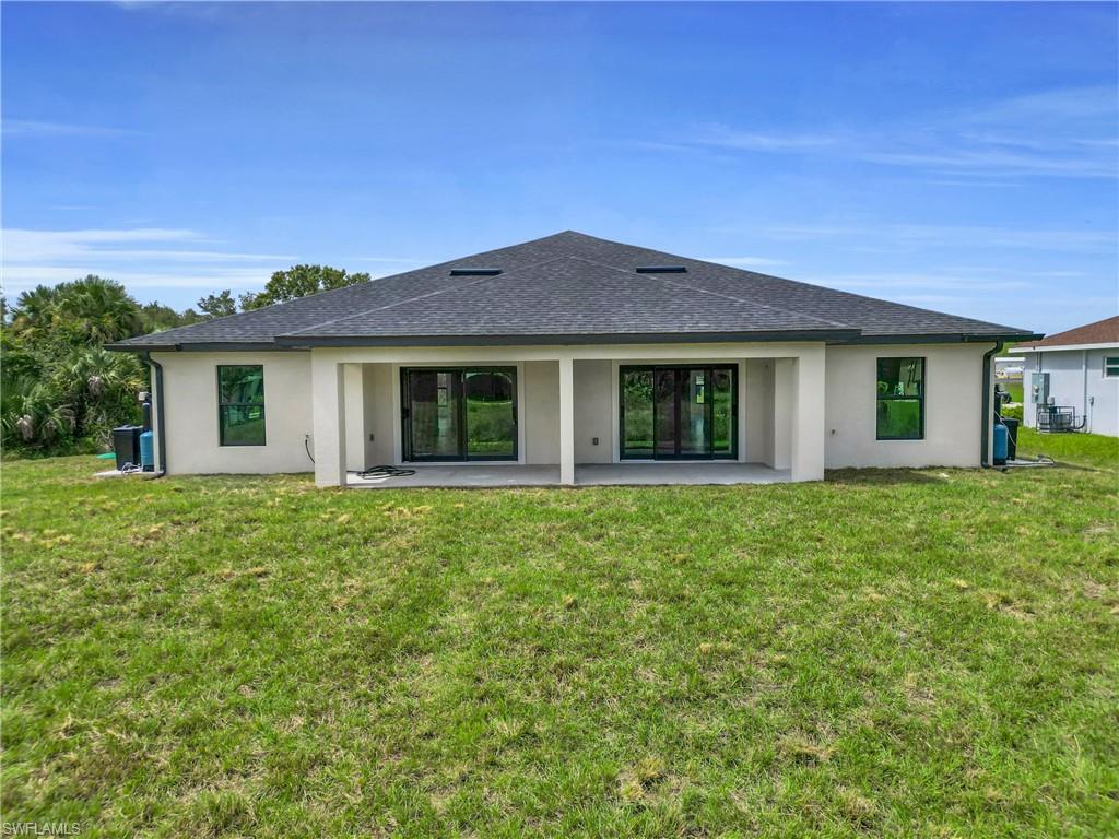Back of property with a shingled roof, stucco siding, a patio area, and a lawn