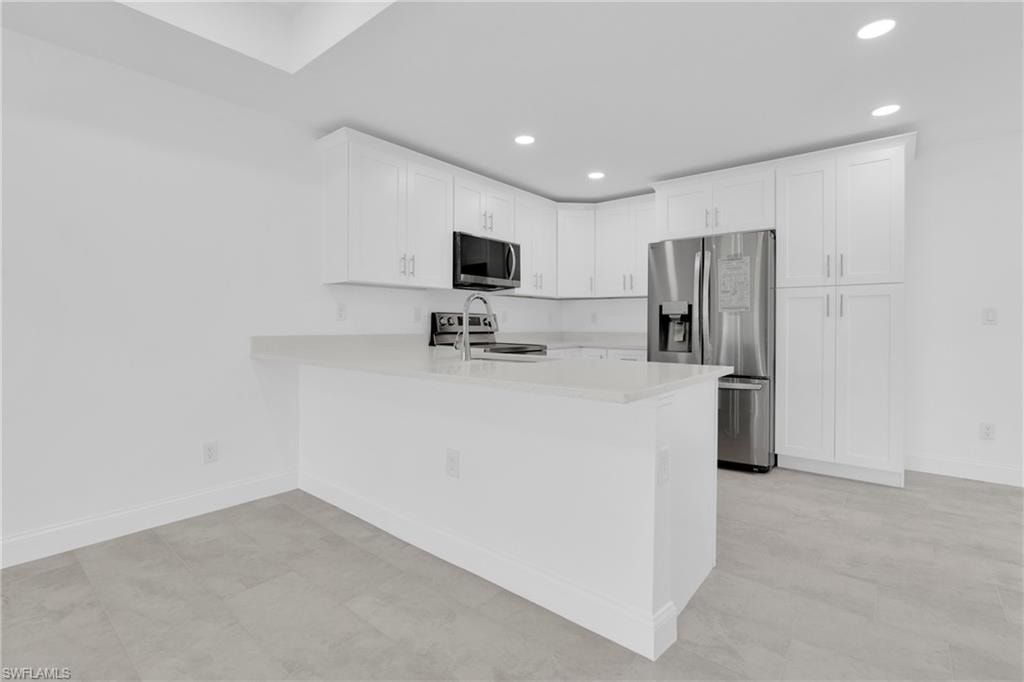 Kitchen with stainless steel appliances, recessed lighting, white cabinetry, a peninsula, and light stone counters