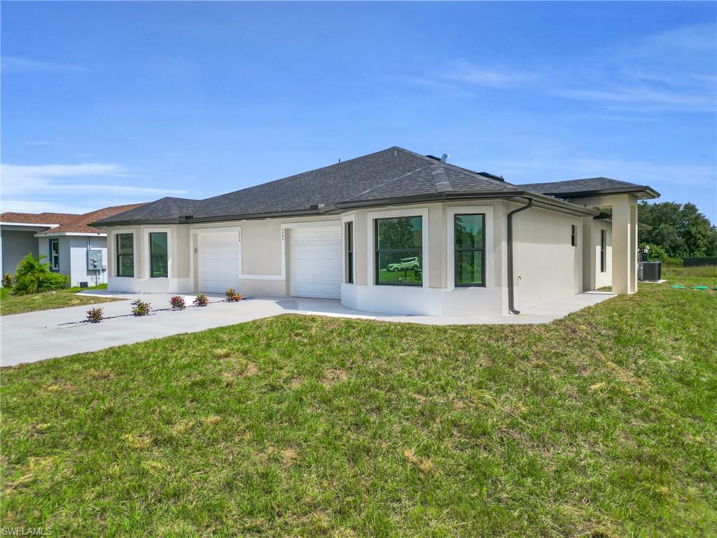 Back of house with stucco siding, a yard, driveway, and roof with shingles
