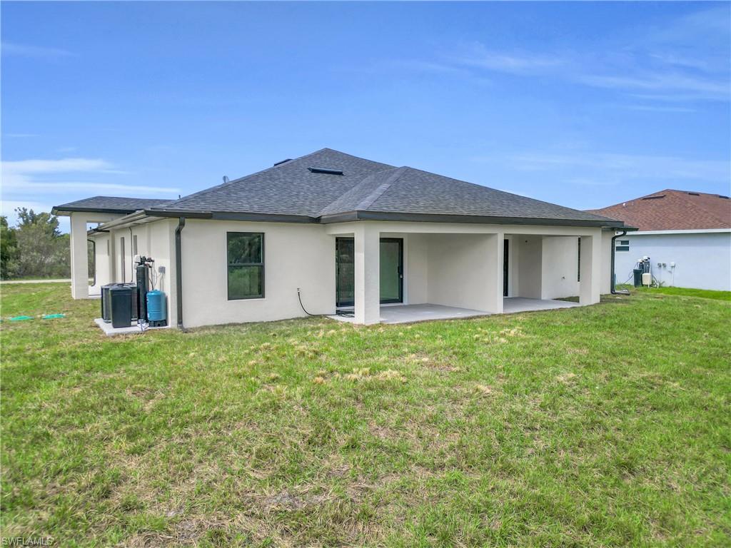 Back of property with a yard, a shingled roof, stucco siding, and a patio area