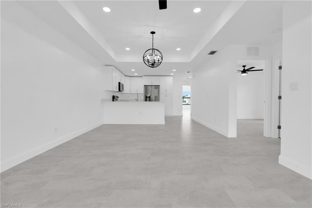 Unfurnished living room with a tray ceiling, recessed lighting, a chandelier, and ceiling fan
