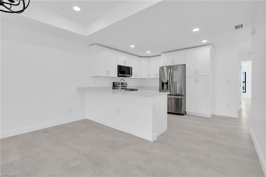 Kitchen with appliances with stainless steel finishes, white cabinetry, recessed lighting, a peninsula, and light stone countertops