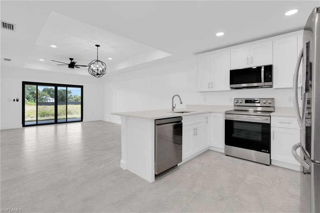 Kitchen featuring appliances with stainless steel finishes, a tray ceiling, recessed lighting, white cabinets, and a peninsula