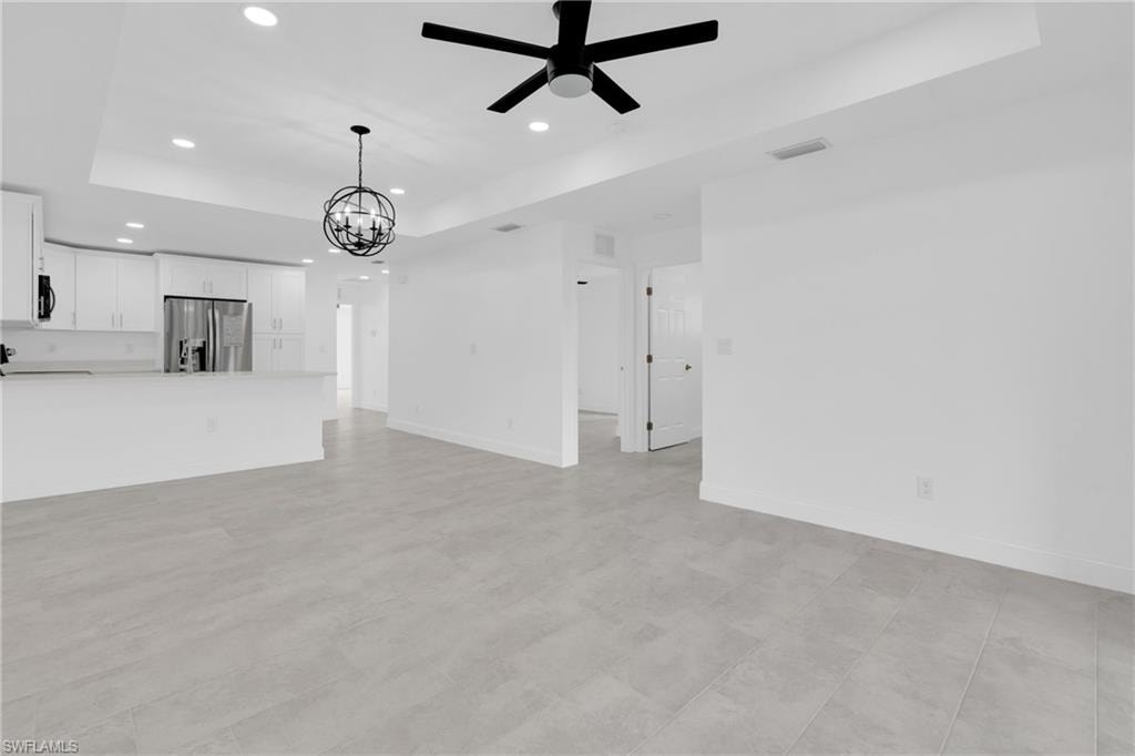 Unfurnished living room featuring a tray ceiling, recessed lighting, a ceiling fan, and a chandelier