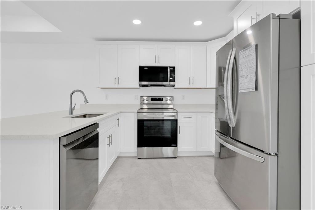 Kitchen with appliances with stainless steel finishes, a peninsula, white cabinetry, light stone counters, and recessed lighting