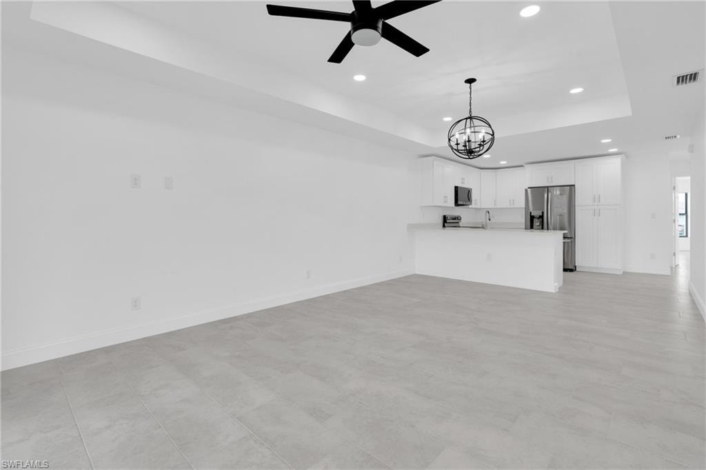Unfurnished living room featuring a raised ceiling, recessed lighting, a chandelier, and ceiling fan
