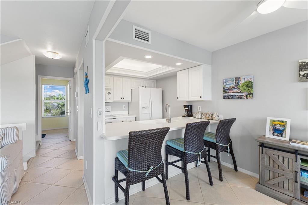 Kitchen featuring white cabinets, light countertops, a kitchen bar, white appliances, and a raised ceiling