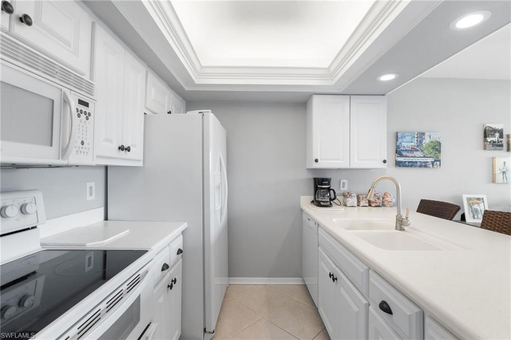 Kitchen with white appliances, white cabinetry, ornamental molding, a raised ceiling, and light tile patterned floors