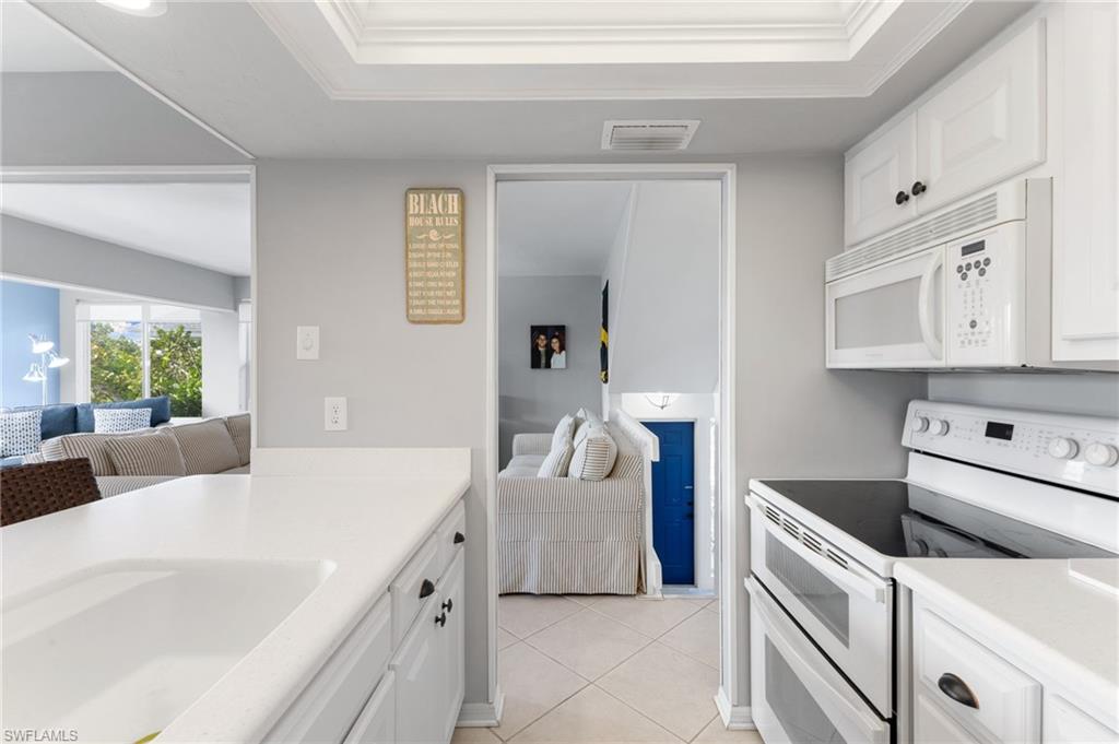 Kitchen with white appliances, white cabinetry, light tile patterned floors, and ornamental molding