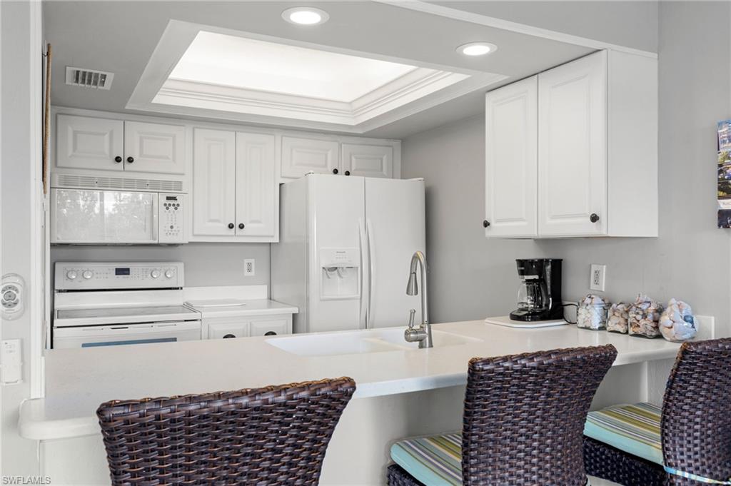 Kitchen featuring a tray ceiling, white appliances, white cabinets, a peninsula, and crown molding