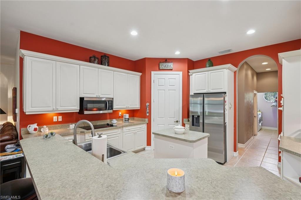 Kitchen featuring arched walkways, white cabinets, appliances with stainless steel finishes, light tile patterned floors, and recessed lighting