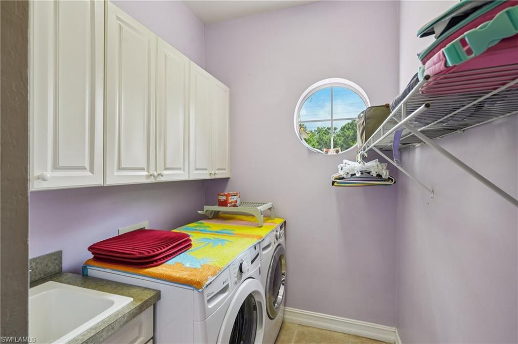 Laundry room featuring washing machine and dryer, light tile patterned floors, and cabinet space