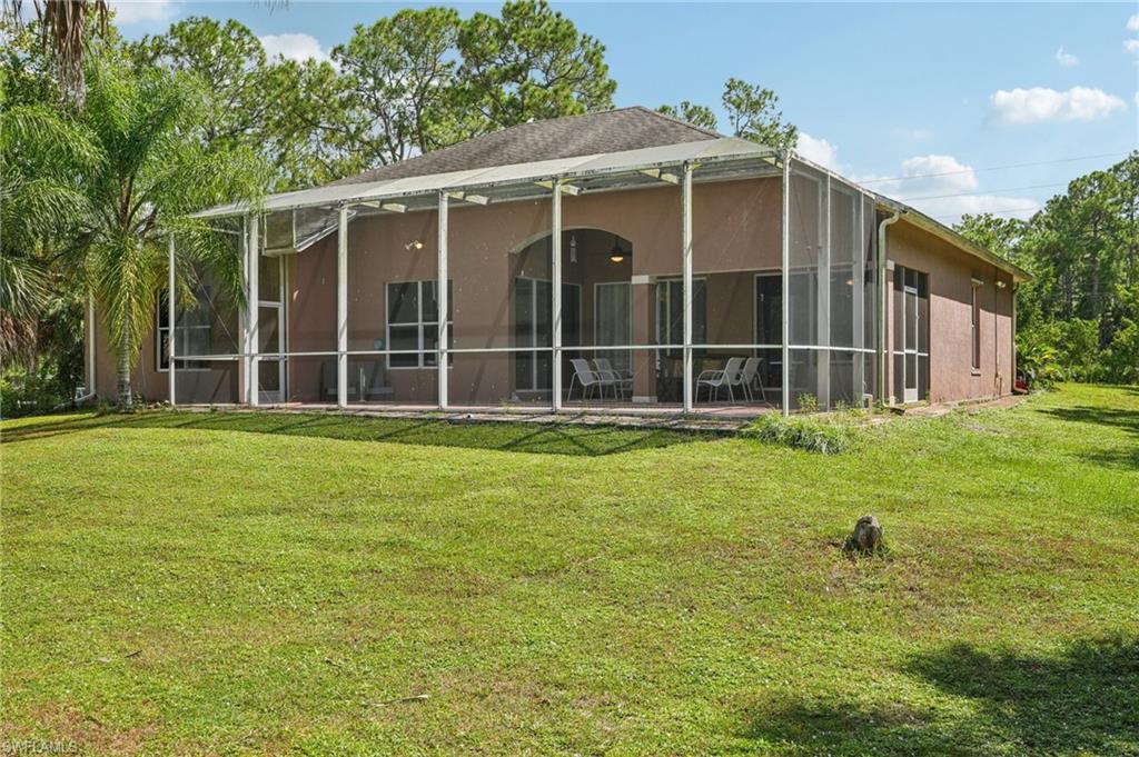 Rear view of house with a yard, stucco siding, a sunroom, and glass enclosure