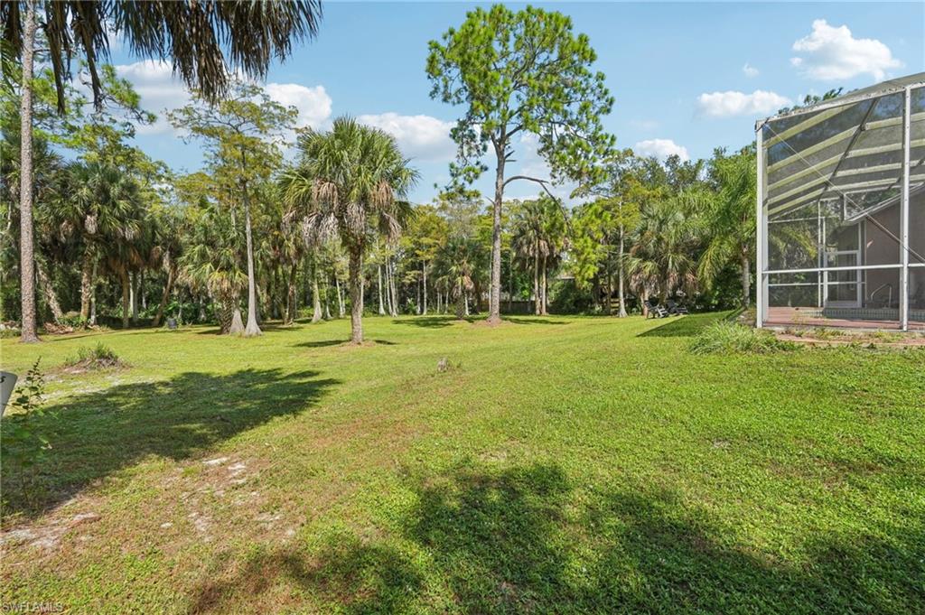 View of green lawn with a lanai, a sunroom, and view of scattered trees