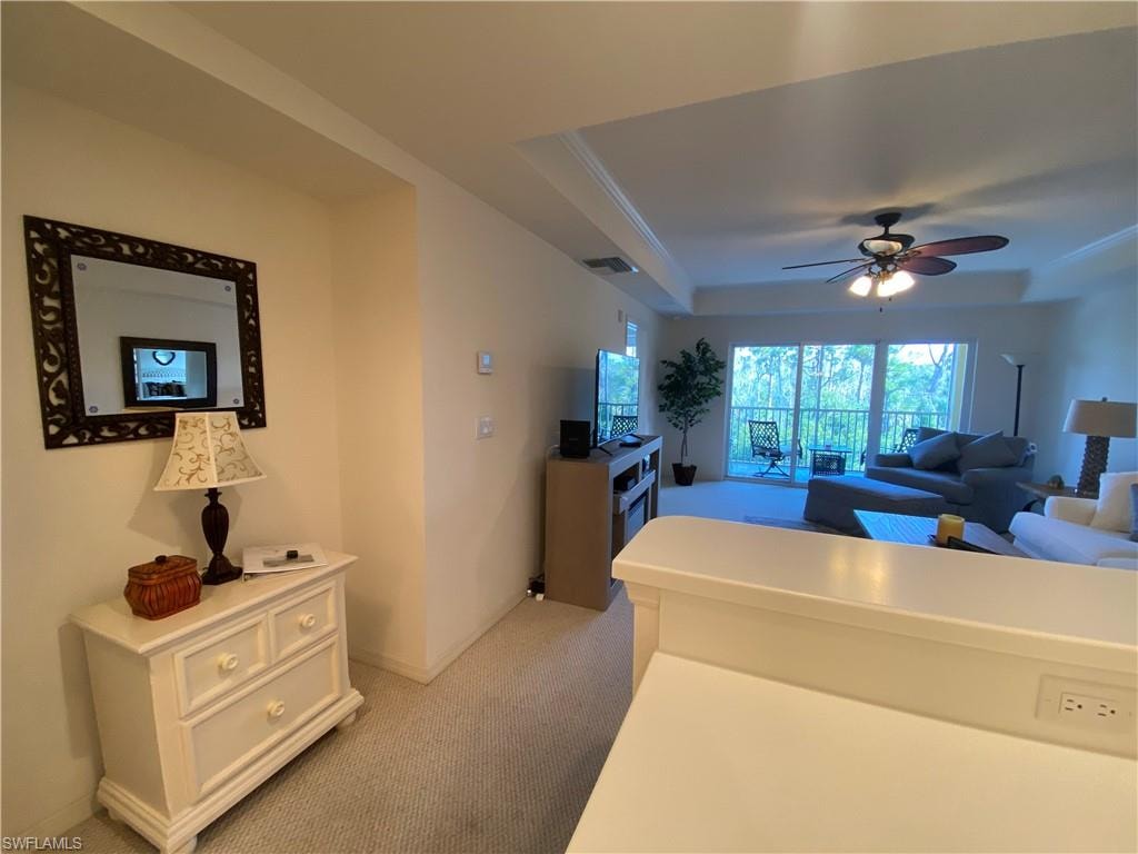 Living room with light carpet, plenty of natural light, a tray ceiling, ceiling fan, and ornamental molding