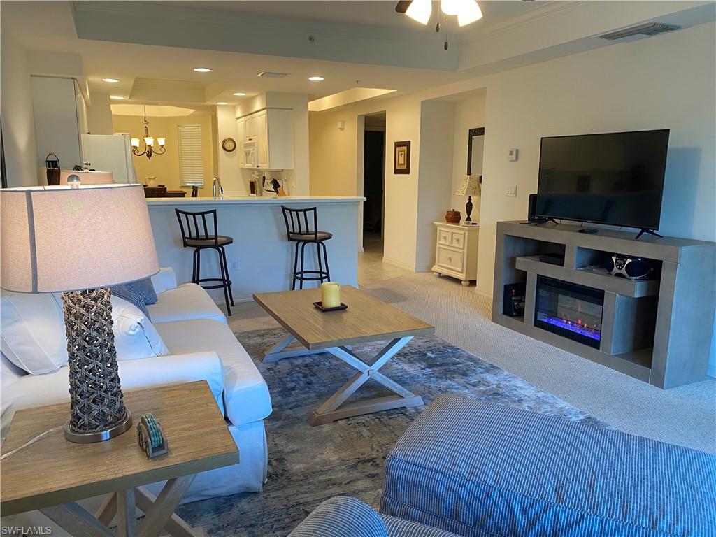 Carpeted living room featuring a tray ceiling, recessed lighting, a chandelier, and a glass covered fireplace