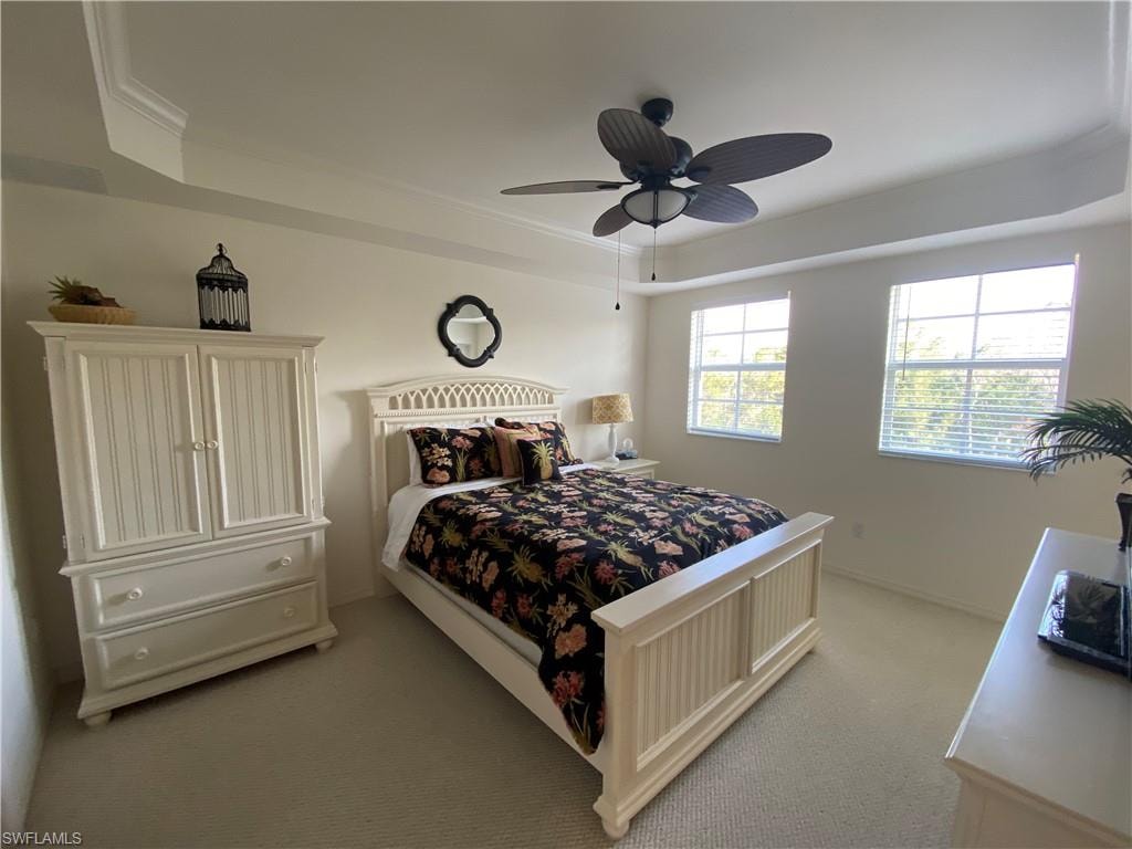 Carpeted bedroom with a raised ceiling, crown molding, and ceiling fan
