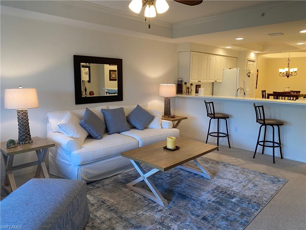 Carpeted living room with crown molding, recessed lighting, a ceiling fan, a tray ceiling, and a chandelier