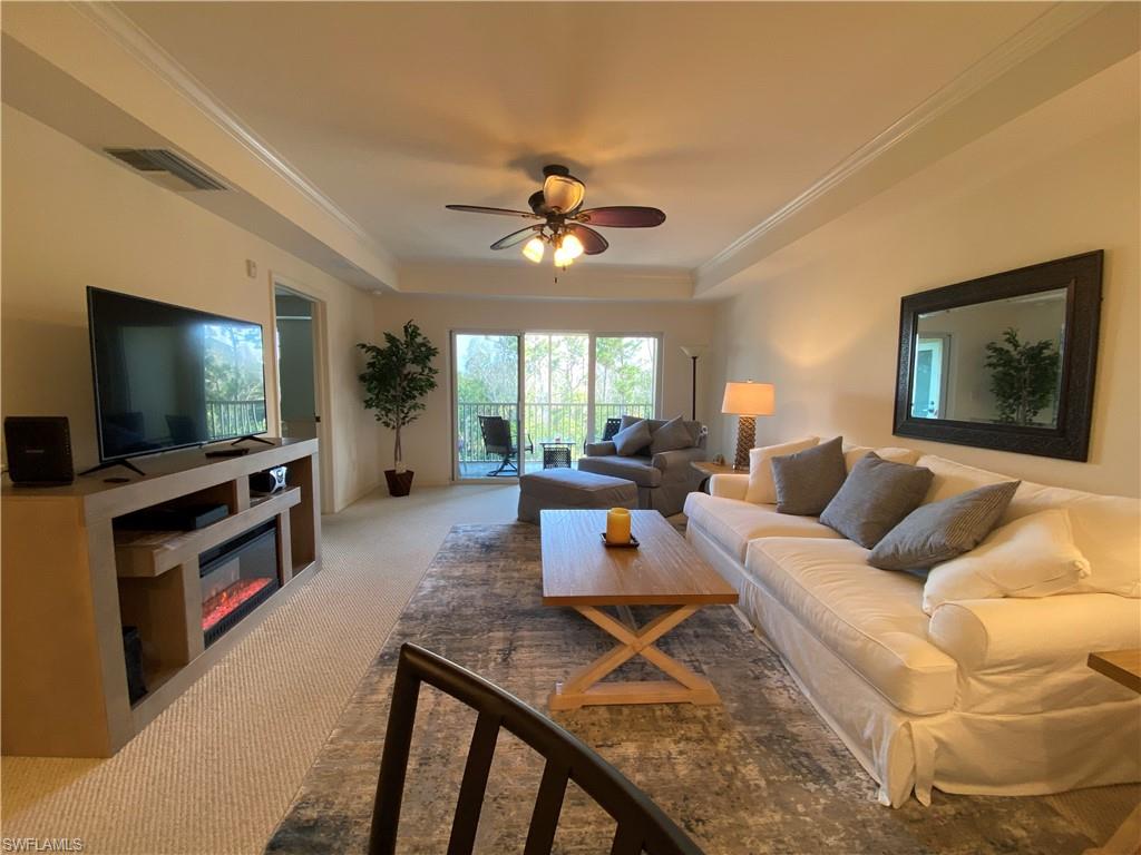 Living room with a raised ceiling, carpet floors, a ceiling fan, ornamental molding, and a glass covered fireplace