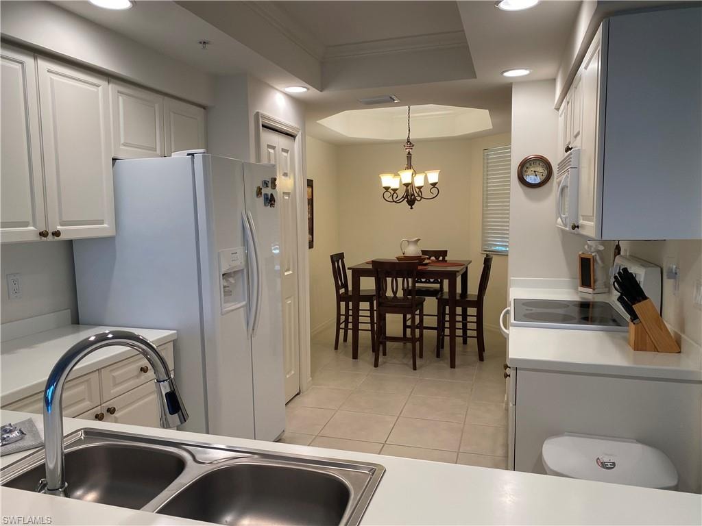 Kitchen with a tray ceiling, white cabinets, white appliances, light countertops, and decorative light fixtures