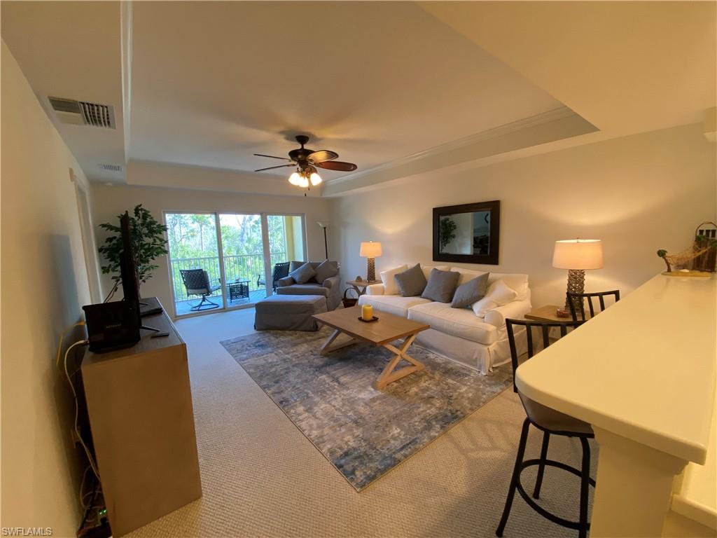 Living area featuring a tray ceiling, carpet floors, and a ceiling fan