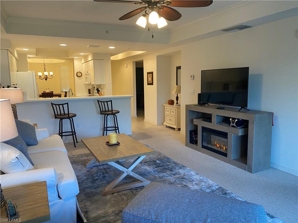 Carpeted living area featuring ornamental molding, a tray ceiling, a glass covered fireplace, a chandelier, and ceiling fan