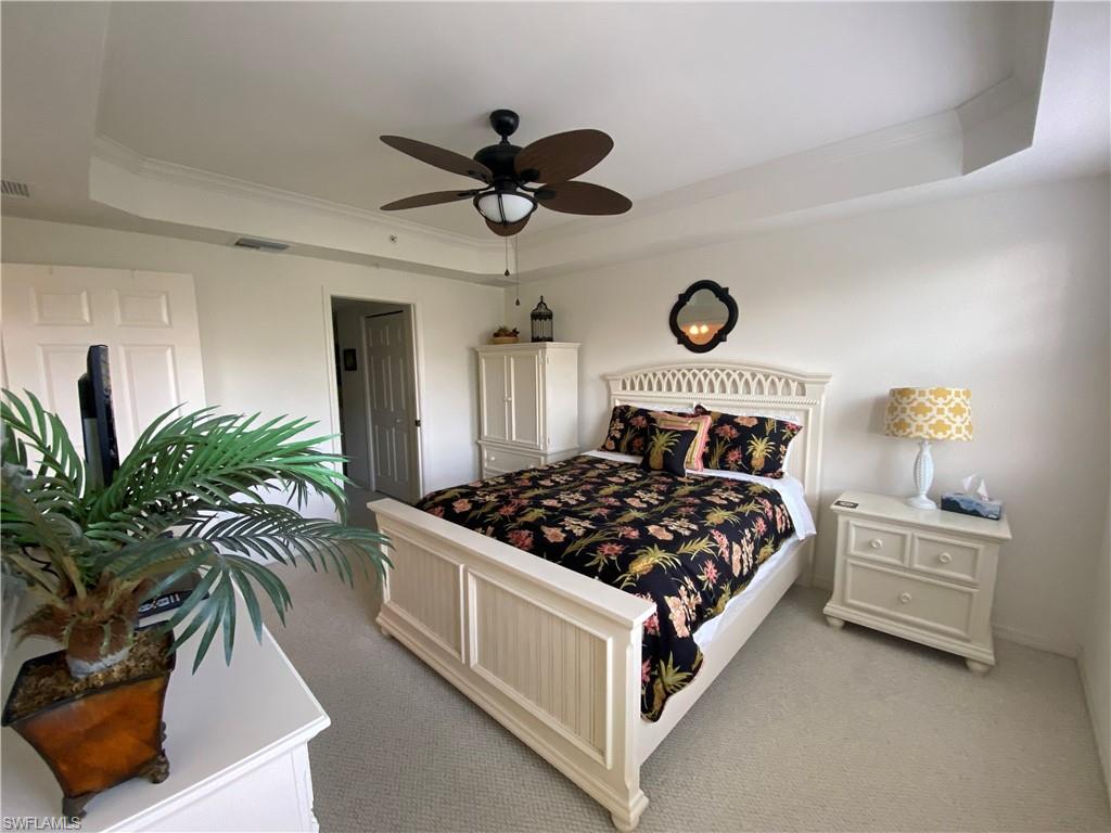 Bedroom with a tray ceiling, light carpet, ornamental molding, and ceiling fan