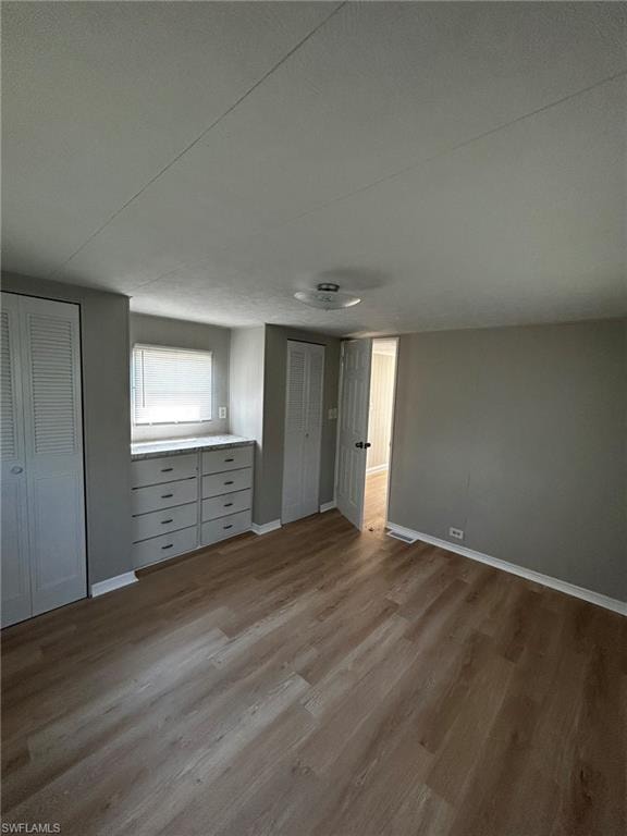 Unfurnished bedroom featuring wood finished floors and two closets
