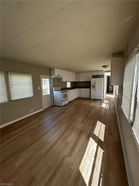 Kitchen with dark countertops, white appliances, white cabinets, dark wood-style flooring, and open floor plan