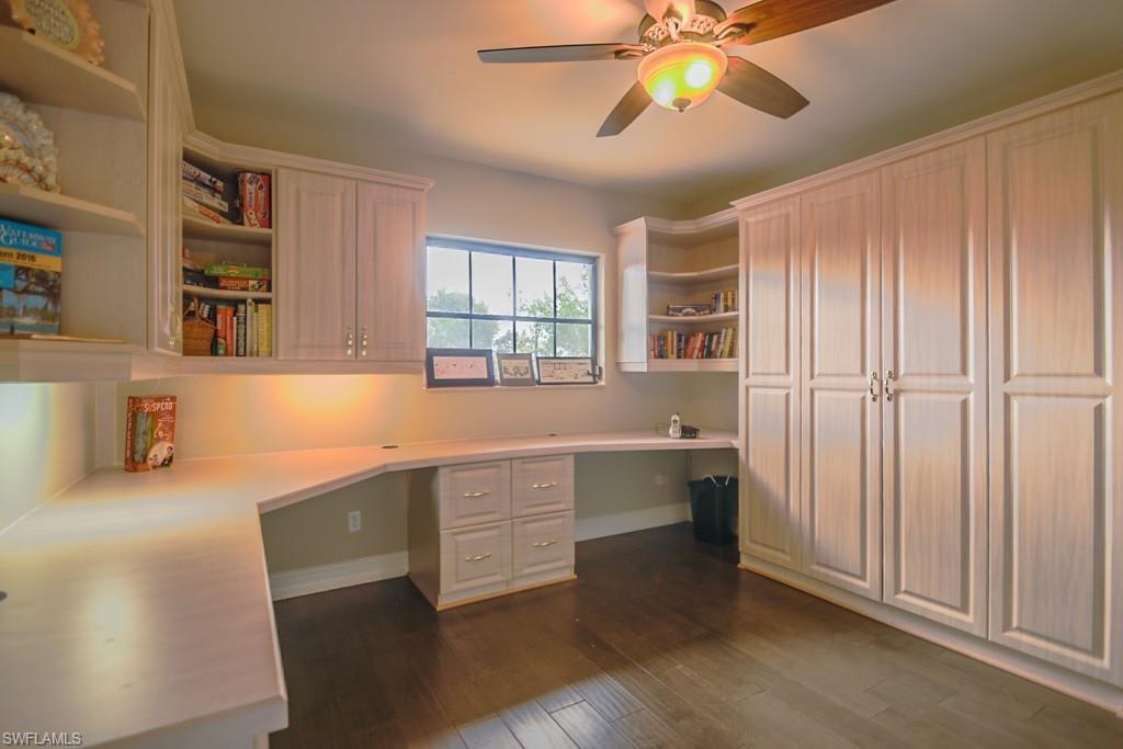 Unfurnished office with ceiling fan, dark wood-type flooring, and built in desk